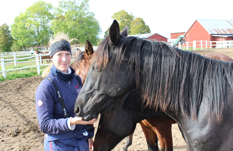 Bild på travtränaren Anna Forssell ståendes vid hennes hästar