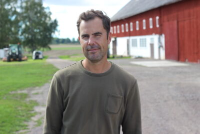 Henrik Egelstig är ansvarig för 200 hektar mark. Han ler mot kameran. En ladugård och en grusväg syns i bakgrunden.