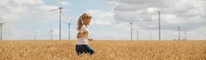 Flicka springer i fält med spannmål. I bakgrunden syns flera vindkraftverk mot en somrig himmel.