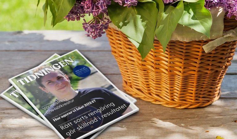 Nytt nummer av tidningen Tidningen ligger på ett bord bredvid en korg med syrenblommor.