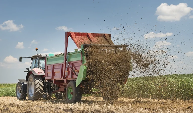Traktor sprider ut fjäderfägödsel på fält.